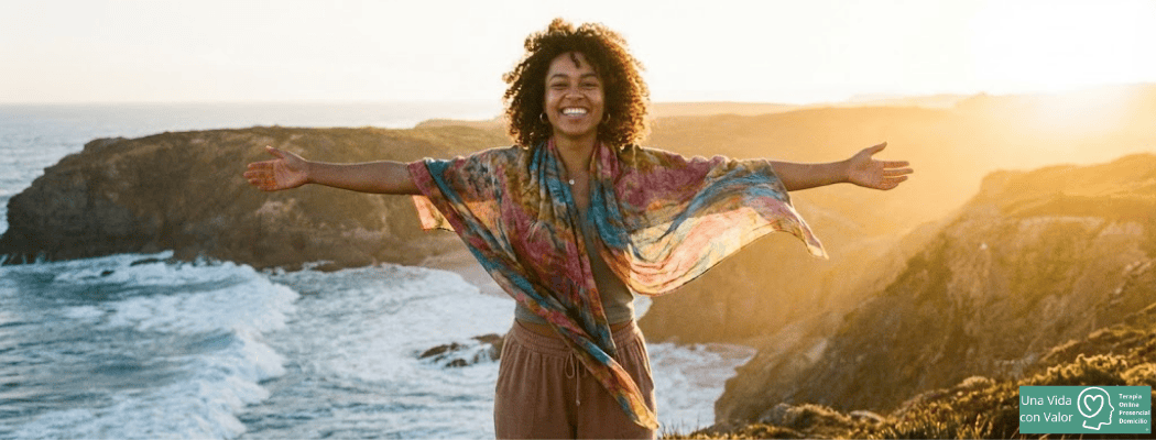 Mujer con los brazos abiertos frente al mar al atardecer, imagen simbólica de autoestima, bienestar y libertad | Una vida con valor